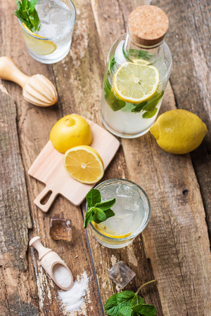 Two glasses of lemonade with with lemon slices, mint and ice on old wooden planksの写真素材