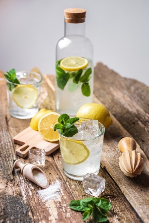 Bottle and two glasses of fresh lemonade with lemon slices, mint and ice on old wooden planksの写真素材
