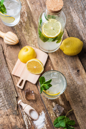 Two glasses of lemonade with with lemon slices, mint and ice on old wooden planks.の写真素材