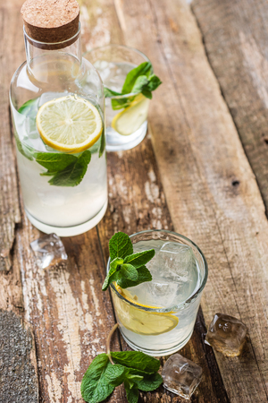 Two glasses of lemonade with with lemon slices, mint and ice on old wooden planks. Close upの写真素材
