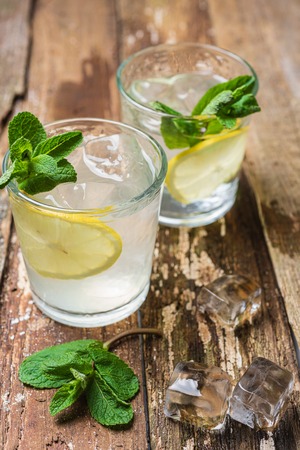 Two glasses of lemonade with with lemon slices, mint and ice on old wooden planks. Close upの写真素材
