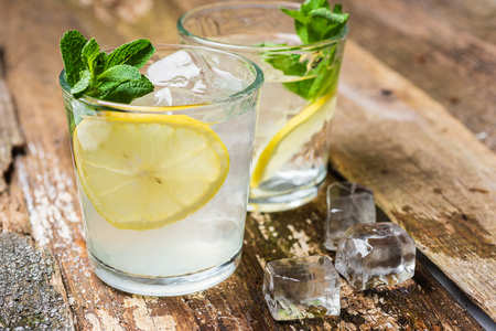 Two glasses of lemonade with with lemon slices, mint and ice on old wooden planks. Close upの写真素材