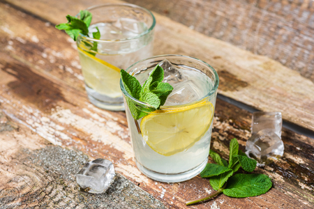 Two glasses of lemonade with with lemon slices, mint and ice on old wooden planks. Close upの写真素材