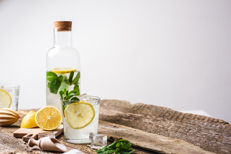 Bottle and two glasses of fresh lemonade with lemon slices, mint and ice on old wooden planks. Copy spaceの写真素材
