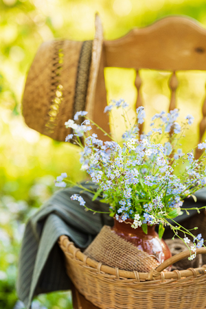 Vintage wooden chair standing in the garden with wicker basket, ceramic vase and bouquet of forget-me-not's on it. Close upの写真素材