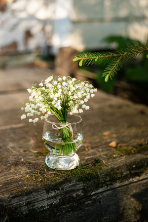 Small bouquet of lilies of the valley in the glass standing on vintage wooden steps in the garden, eveningの写真素材