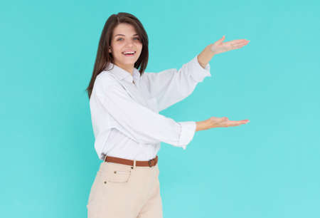 Photo of happy young woman standing isolated over blue wall background. Looking camera showing copyspace between hands.の写真素材