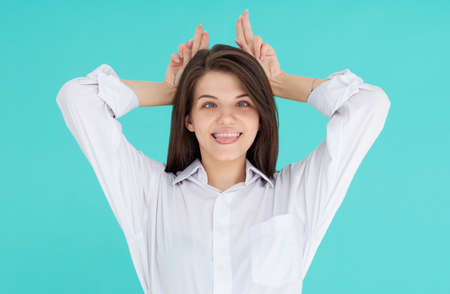 Pretty young woman with tongue out gesturing bunny ears and looking at camera on the blue background.の写真素材