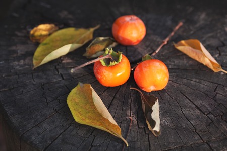 Persimmon fruits and leaves on the dark wooden background, top view.の写真素材