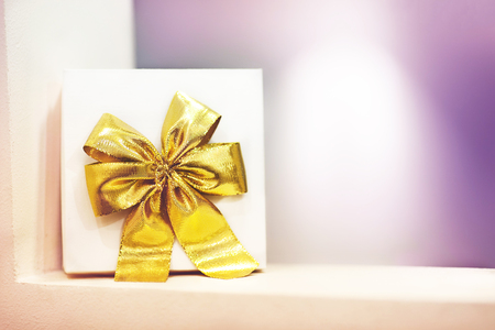 White gift box with a yellow bow is on the shelf on a purple background. There is a place for text.の写真素材
