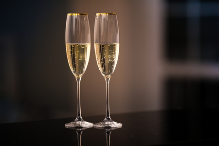 A pair of glasses of champagne in the interior. Festive picture of two wine glasses with sparkling champagne. Closeup of a pair of wine glasses. Dining and night life concept.の写真素材
