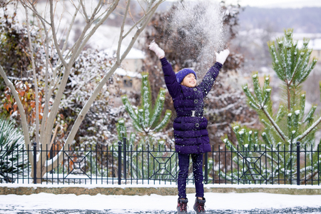 Beautiful young girl in the violet clothes playing with snow outdoor.の写真素材