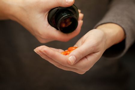 Womans hands with pills on, spilling orange pills out of bottle on dark background.の写真素材