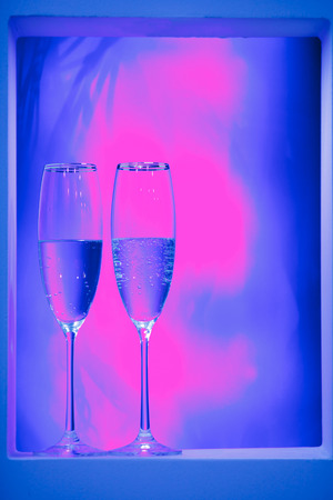 Holiday pair of glasses of champagne in the interior. Blurred luminocity neon color backdround. Holiday pair of glasses of champagne in the interior. Blurred luminocity neon color backdround. Sent Valentines Day and night life holiday concept.の写真素材