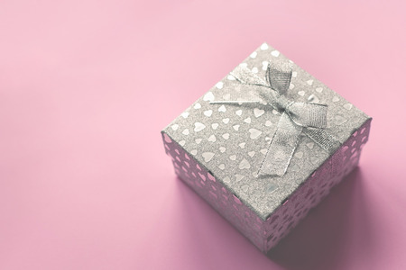 Festive picture of silver gift box with a bow and small hearts on the gentle pink background. Holiday atmosphere. Sent Valentines day and wedding holidays concept.の写真素材