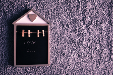 Little decorate wooden house with black copy space ahd small clothespins on the grey wool background. White words Love is on the writing board.の写真素材