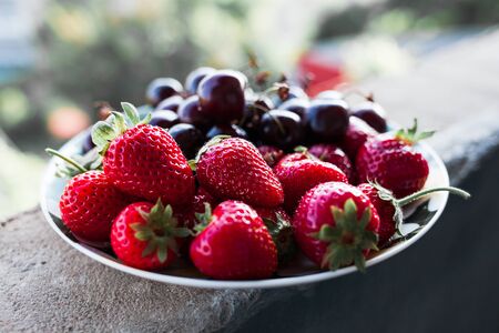 Organic sweet cherry and strawberry on a white plate. Healthy food, vitamins. summer lunch. top view on a balcony, selective focus.の写真素材