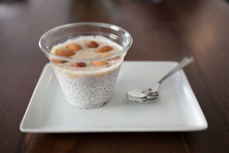 Dessert yogurt mousse. Healthy bowls of yogurt and Chia seeds and almond nuts. Womens hand holding a white plate with breakfast.の写真素材