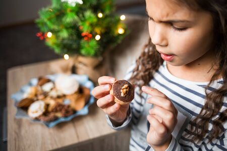 Little girl eating Christmas cookies. New year tree on background.の写真素材