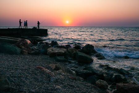 Sunset on the sea beach with fishermen on horizon. Romantic beautiful view.