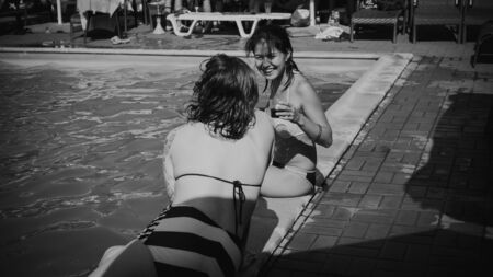 Employees of IT companies , the summer of 2018. Two young girls in bathing suits drink cocktails by the pool and laugh, black and white photo.Editorial, illustrative, illustrative editorのeditorial素材