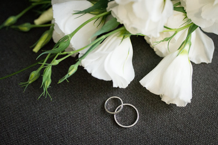 White golden wedding rings on grey background with white flowers closeupの写真素材