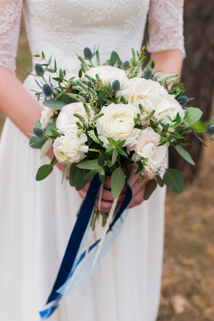 Bridal bouquet with white roses. Wedding. The bride in white wedding dress holds a wedding bouquet with white roses and greenery decorated with long silk ribbonの写真素材