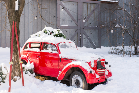 Old red car with Christmas tree branches on the roof in the snow-covered yard on a grey backgroundの写真素材