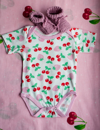 Clothes for newborns with cherries and baby's pink bootees on the bedclothes with cherriesの写真素材