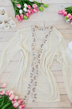 Women's white lingerie with beige dressing gown on a wooden floor with candles and tulipsの写真素材