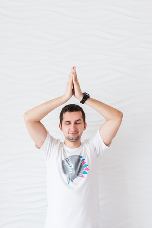 Young man in white t-shirt makes meditation on exercise pilates yoga on a white backgroundの写真素材