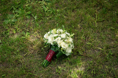 White wedding bouquet with roses, chamomile and red ribbon lies on a grassの写真素材