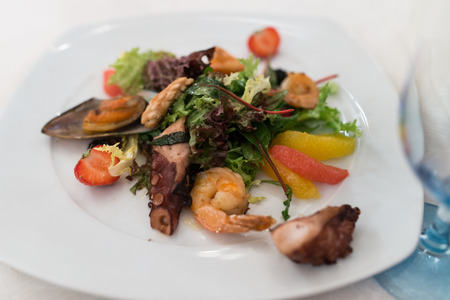 Salad with seafood, octopus, strawberry, citrus and greens into the white plateの写真素材