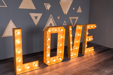 A wooden lettering Love with light bulbs on a grey background.のeditorial素材