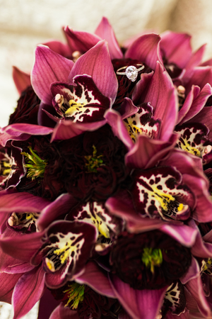 Ring with diamond lying on a wedding bouquets with red orchids. Wedding detailsの写真素材