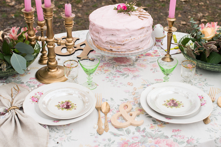 Wedding table. Vintage white plates with roses on a table with cutlery and glasses. Pink wedding cake with rose on the top on the banquet tableの写真素材