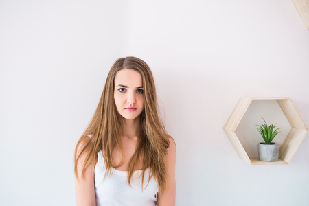 Indoor portrait of gorgeous beautiful young female model with perfect healthy skin and brown long hair staring at camera with serious thoughtful look, dressed in white singletの写真素材