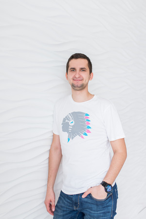 Young smiling man in white T-shirt and blue jeans on a white background looking at cameraの写真素材
