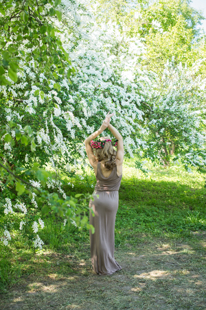 Slim young girl in a brown sundress and a wreath of roses on a background of white bloomingの写真素材