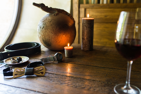 Men's rings in bronze plate, watch and a glass of wine on a wooden table with burning candles. Men's accessorizes, necktie, belt, watchの写真素材