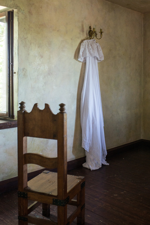 Beautiful white rustic wedding dress hanging on the chandelier in the roomの写真素材