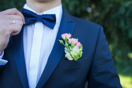Stylish groom in blue jacket, white shirt with white and pink boutonniere. A golden wedding ring on a groom's finger.の写真素材