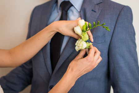 Preparations the groom for the wedding. Bride puts on boutonniere on groom's jacket. Romantic wedding momentの写真素材