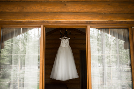 White lush wedding dress hanging on the hanger in the room view from the street. Bridal gown.の写真素材