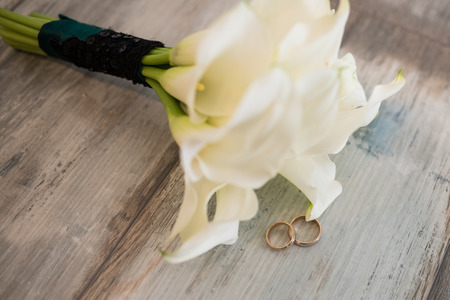 Two golden rings on the wooden background near the white wedding bouquetの写真素材