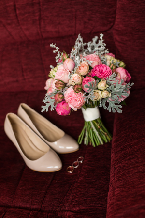Wedding bouquet with purple and pink roses. Wedding accessories are lying on a red armchairの写真素材