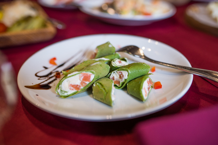 Green pancakes. Pancakes with spinach stuffed with cream cheese and fish on a white plate.の写真素材