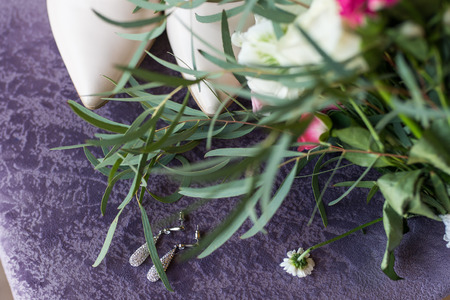 Wedding beige shoes and a bridal earring with gemstones lying on the lilac background. Wedding accessories.の写真素材