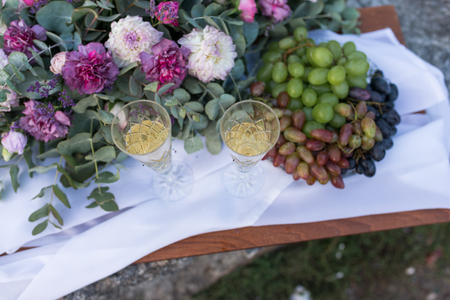 Romantic dinner outdoors. Glasses with champagne, grapes and a lot of flowers on a wooden board.の写真素材
