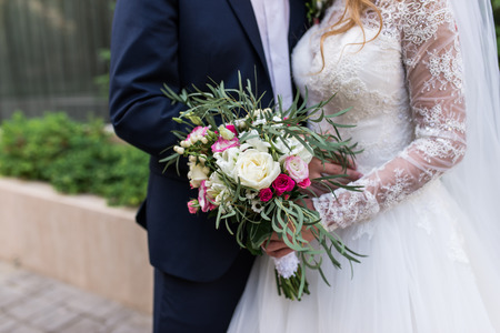 Wedding. The girl in a white dress and a guy in a suit are holding a beautiful bouquet of white and pink flowers and greenery. Wedding lush rustic bouquet. Wedding detailsの写真素材